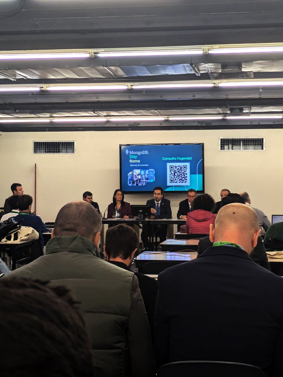 Tavola Rotonda CRUI e Sourcesense al MongoDB Day Roma 2024, con relatori e relatrici seduti a discutere davanti a un pubblico. Sullo schermo, il titolo 'MongoDB Day Roma' e un QR code per accedere all'agenda dell'evento.