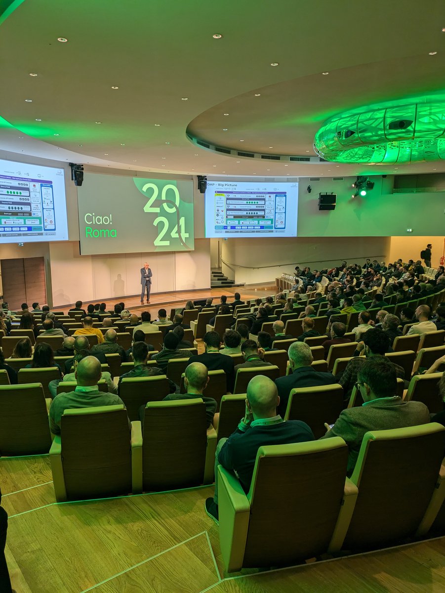 Sessione plenaria al MongoDB Day Roma 2024, con un relatore che parla sul palco davanti a una platea. Sullo schermo si legge 'Ciao! Roma 2024' con dettagli tecnici visibili nelle slide proiettate.